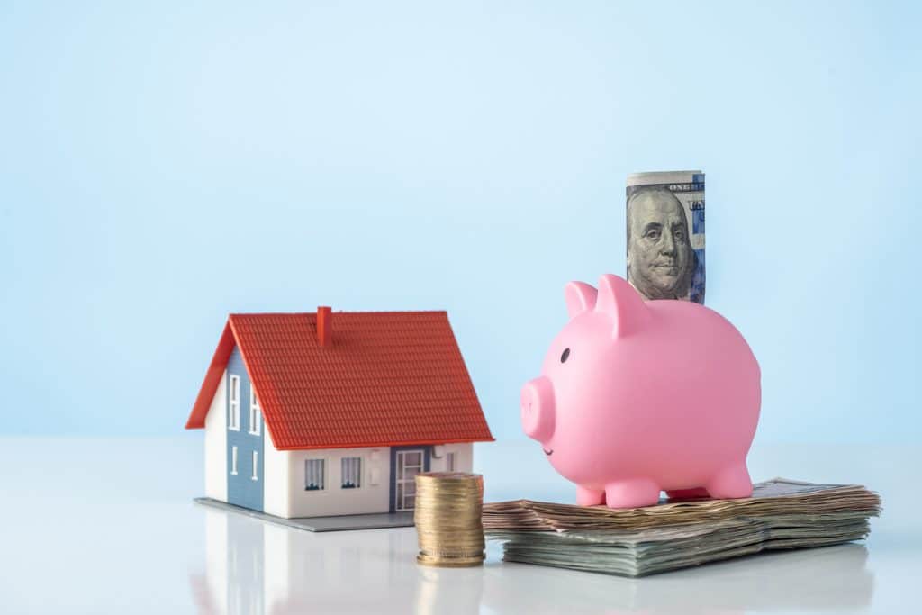 Concept of real estate investing with house model and piggy bank