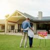 Shot of a couple standing next to a real estate sold sign at their new house