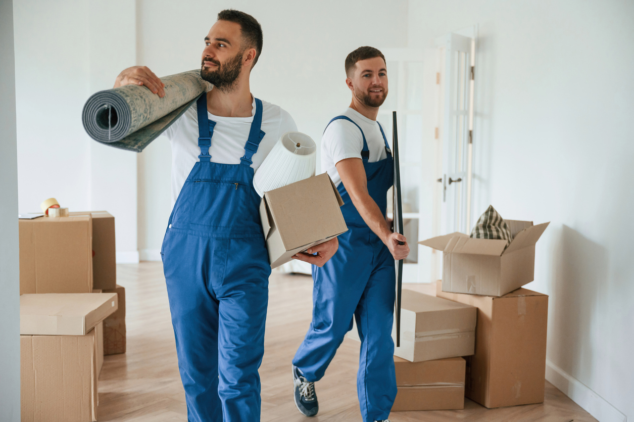 Mat and painting in hands. Two moving service employees in a room