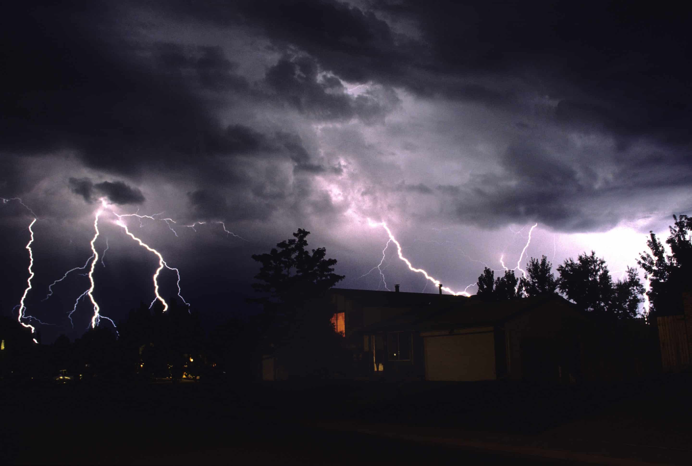 Four lightning strikes over houses and trees in Denver