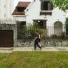 People walk past a white house and fence in a residential neighborhood.