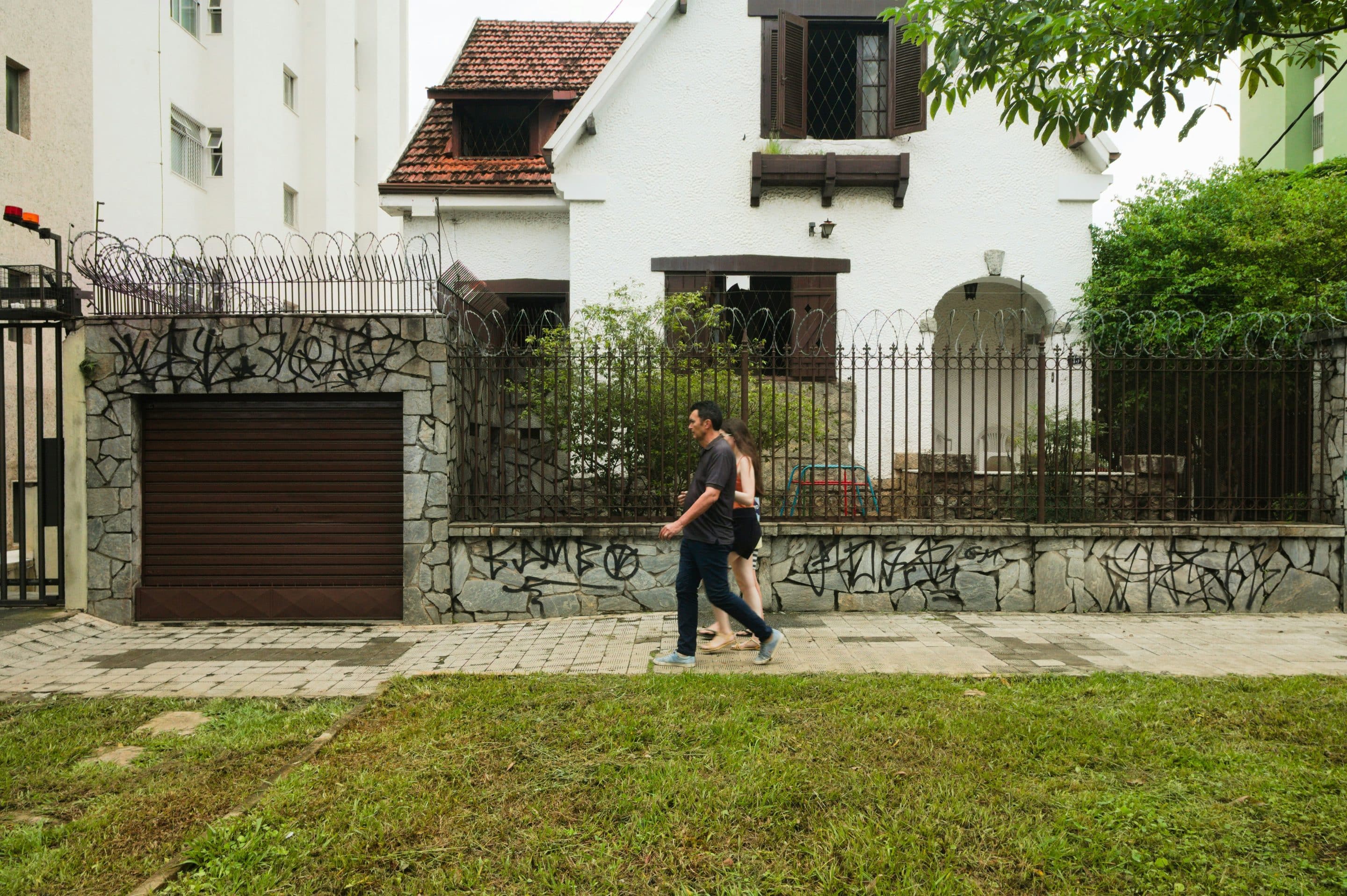 Homebuyer Demand as Mortgage Rates Rise — Illustrative People walk past a white house and fence in a residential neighborhood.