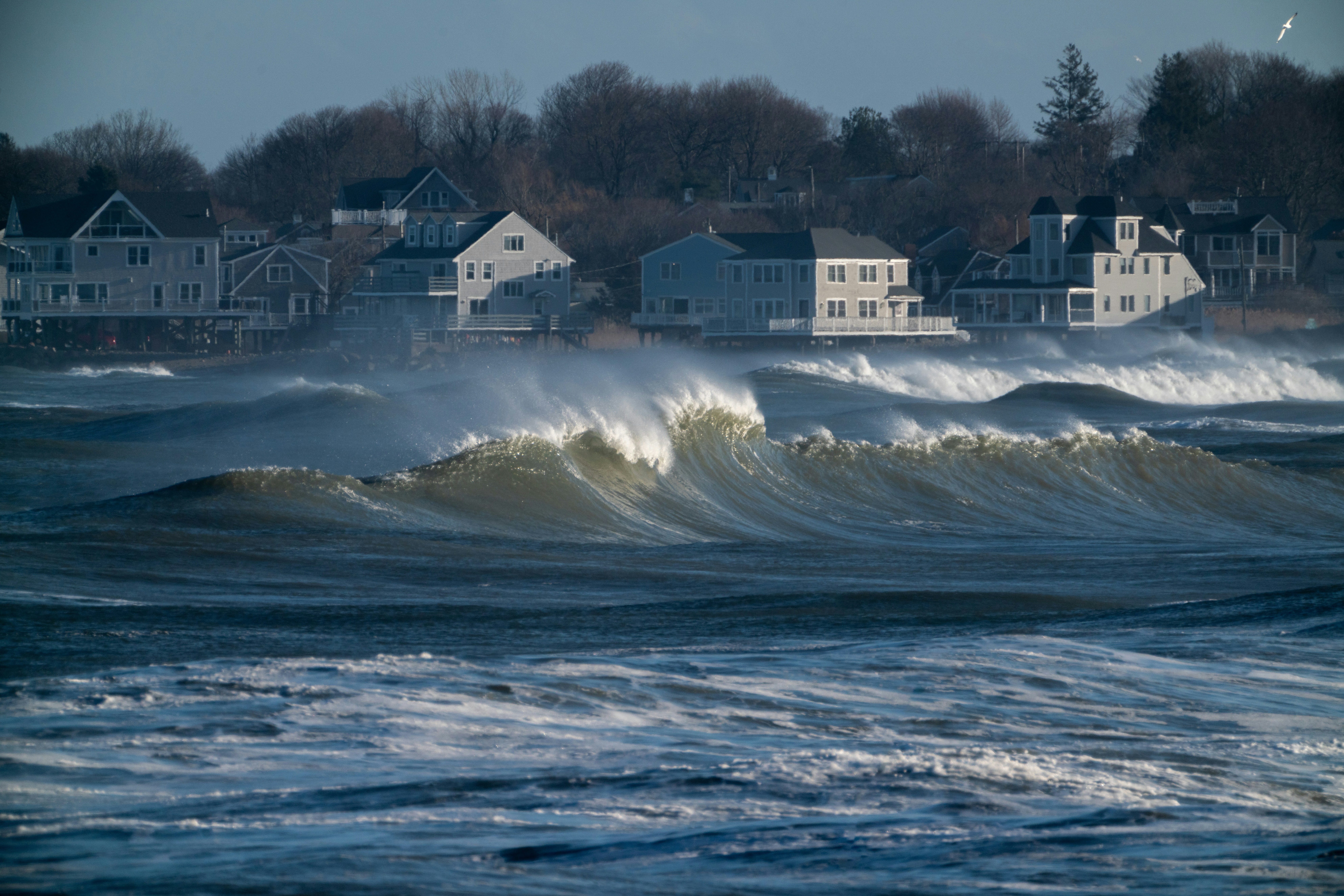 Large ocean wave breaking near waterfront houses; illustrative photograph, not the Long Beach storm