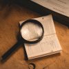 Magnifying glass on printed pages, representative illustration of document review and fraud screening